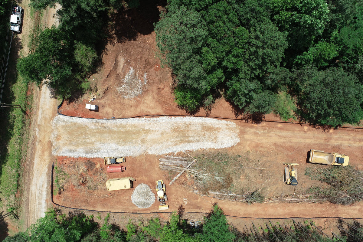 Overhead view of an active road construction site with earthmoving equipment beside a forest.
