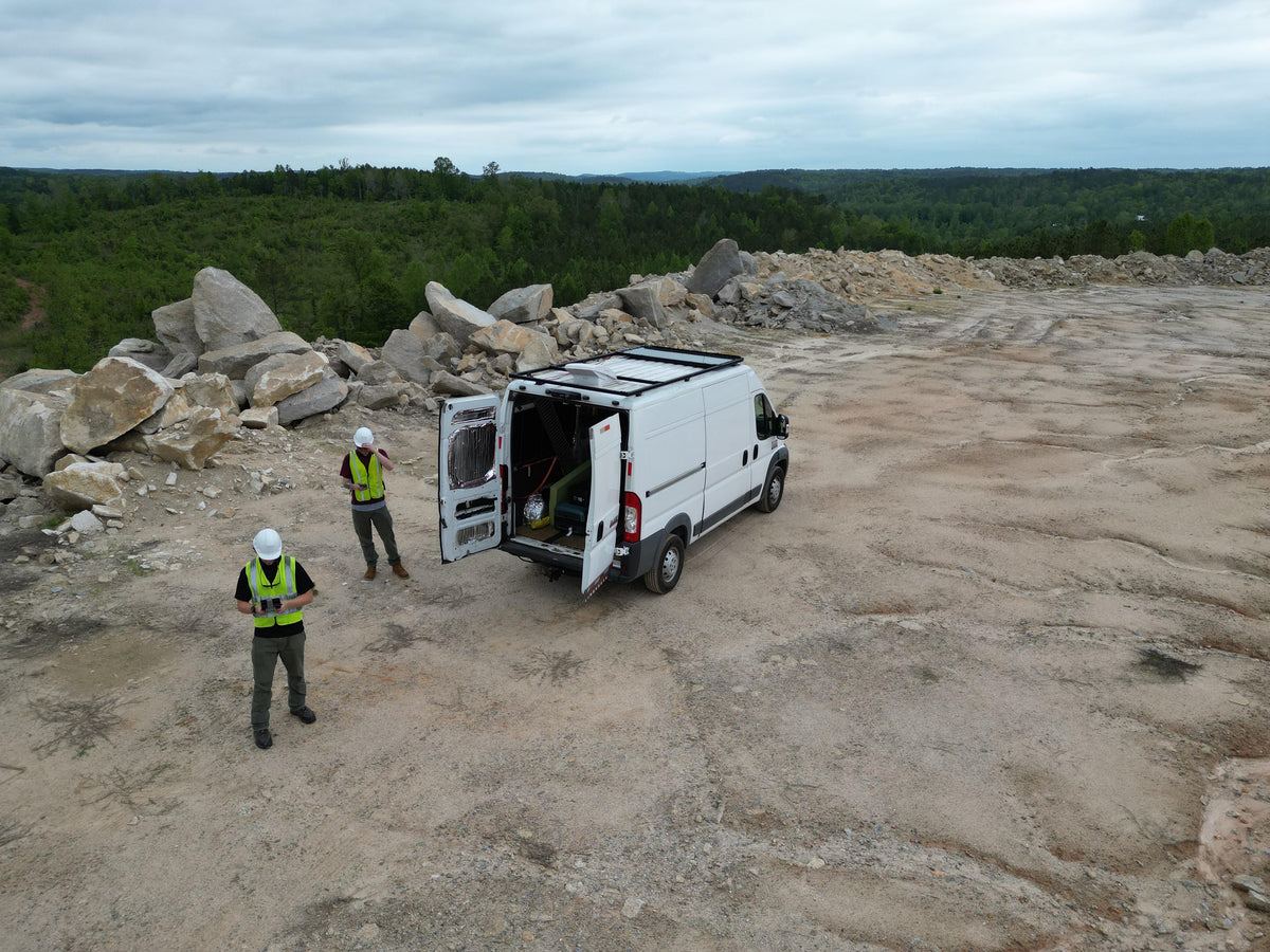 Movement Motion field team wearing high-visibility vests and hard hats beside a survey vehicle at a quarry.